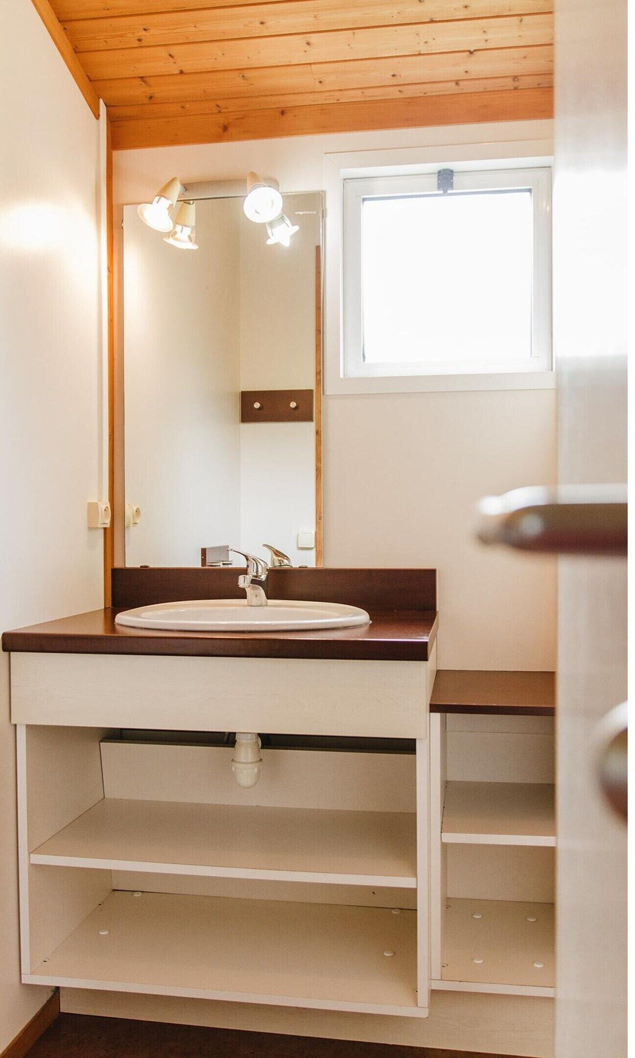 Ein Badezimmer mit Holzboden, einem weißen Waschbecken, einem Spiegel und einem Fenster.