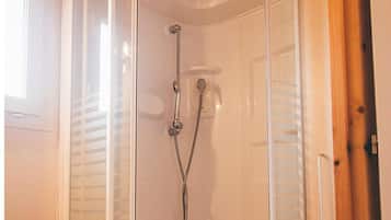 A glass-enclosed shower stall with a white toilet, wooden ceiling, and a small shelf unit.