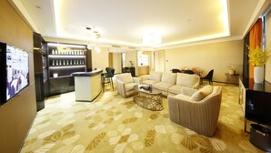 Una sala de estar moderna con sofá, mesa de centro y televisor. Se observa una zona de bar con botellas y una pantalla de televisión.