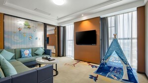 Habitación de hotel con sofá modular, televisor de pantalla plana, una tienda de campaña y un ventanal grande.