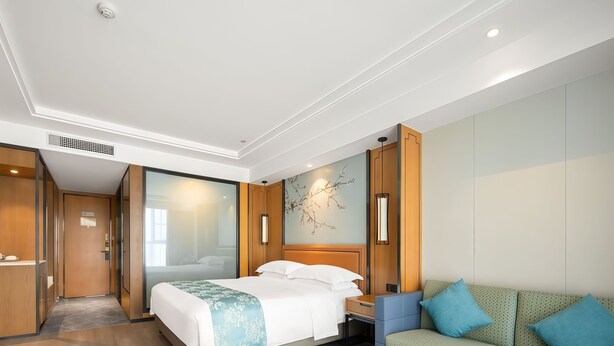 Una habitación de hotel con cama, sofá, mesa y una obra de arte colgada en la pared.
