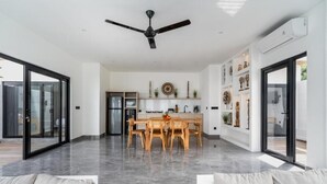 Amplia sala de estar con mesa de comedor, ventilador de techo y cocina al fondo.