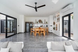 A spacious living area with a dining table, a ceiling fan, and a kitchen in the background. - Majys 1 Villa by Tasvan (Badung)