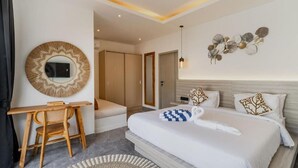 Una habitación de hotel moderna con una cama grande, un escritorio, una silla, un espejo redondo y una obra de arte en la pared.