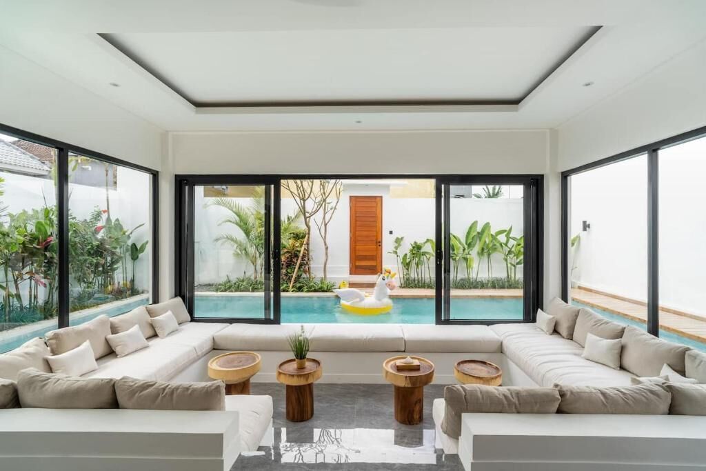 Ein modernes Wohnzimmer mit Blick auf einen Pool, großen Fenstern und einer Sofagarnitur.