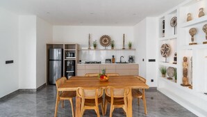Cocina moderna con armarios blancos, un refrigerador de acero inoxidable y un comedor con mesa de madera y sillas de mimbre.