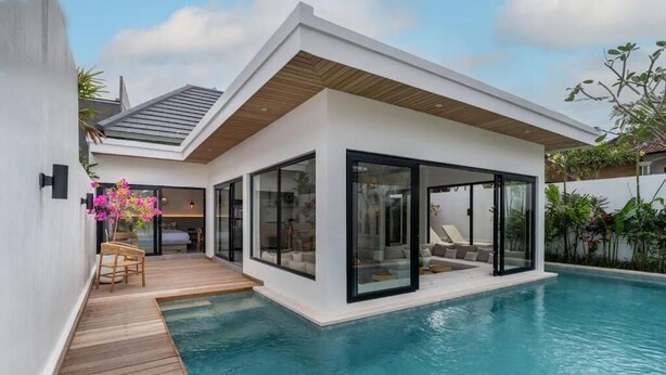 Una casa moderna con piscina, amplios ventanales de vidrio y una terraza de madera.