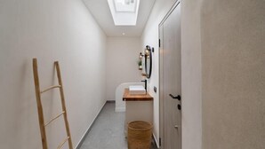 Un pasillo estrecho con tragaluz, una escalera de madera, un lavamanos pequeño y una cesta de mimbre.