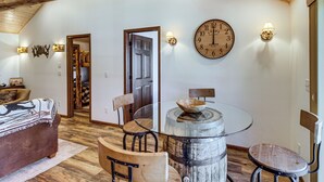 Un intérieur chaleureux avec un plafond en bois, une table ronde entourée de chaises, une grande horloge murale et un centre de table rustique en forme de tonneau.