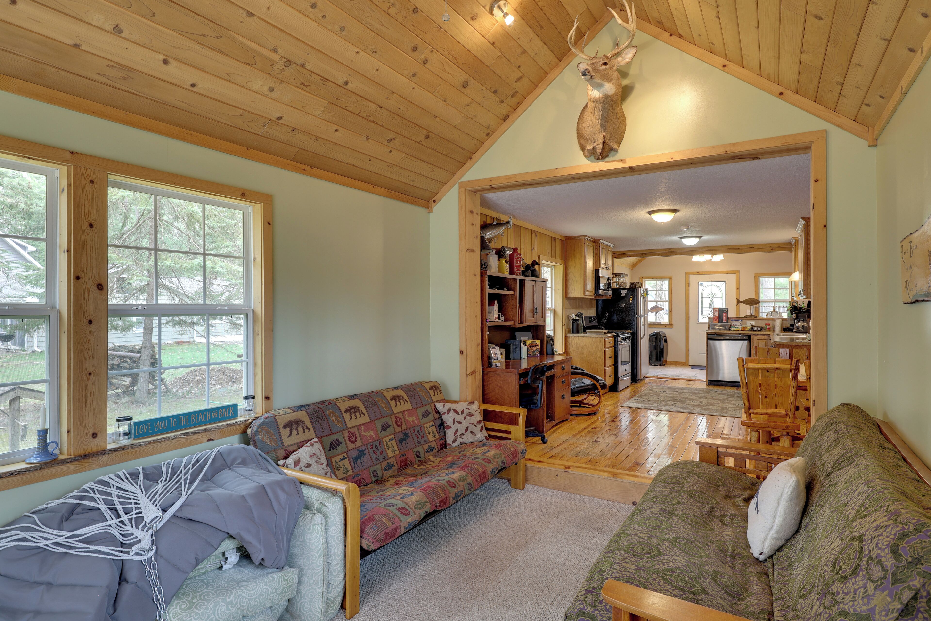 A cozy cabin interior with a wooden ceiling, a sofa, a dining table, and a kitchen area.