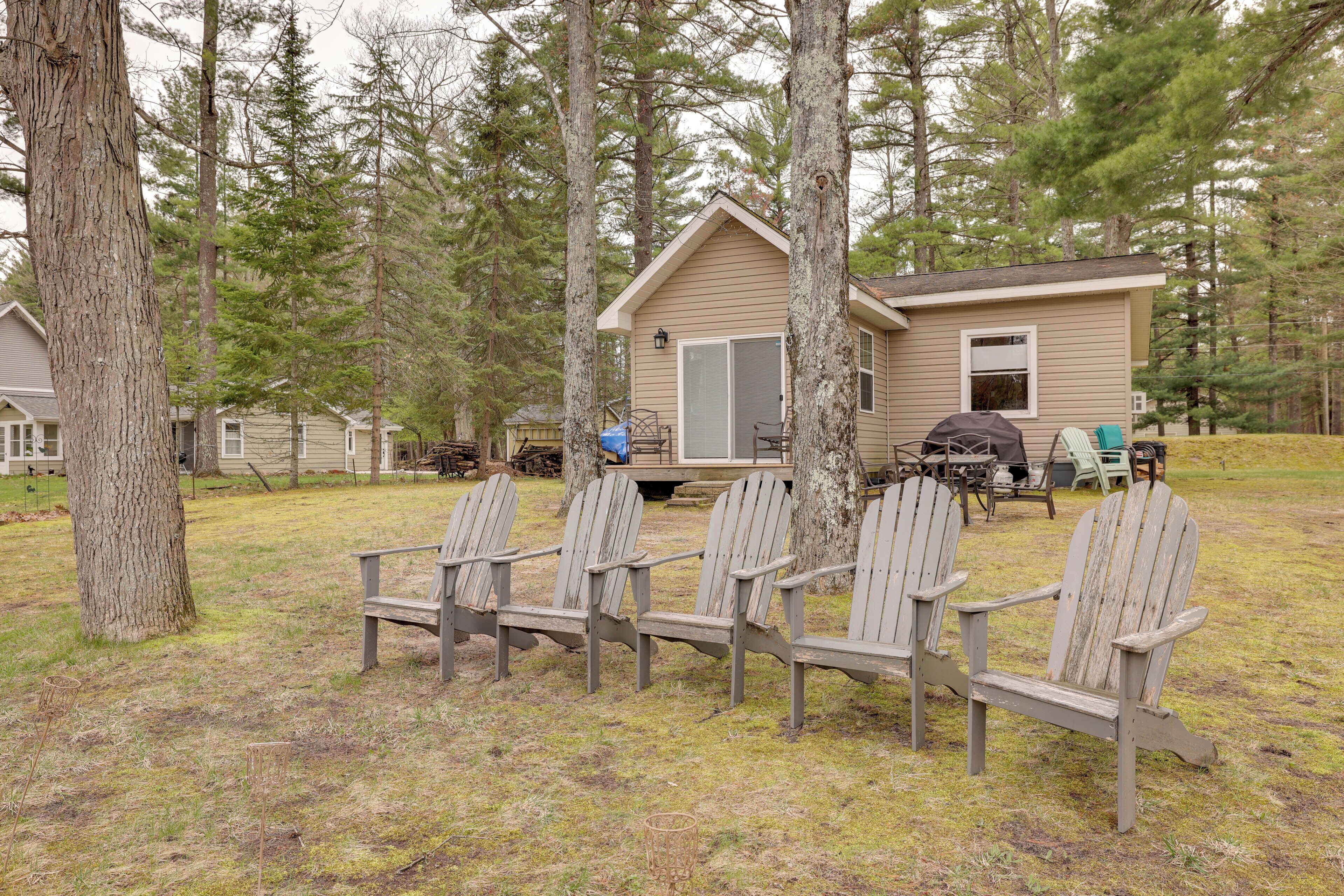 Uma cabana com varanda, rodeada por árvores, e quatro cadeiras Adirondack na frente.