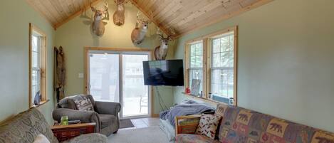 A cozy living room with wooden ceiling beams, a flat-screen TV, and deer antlers on the wall.