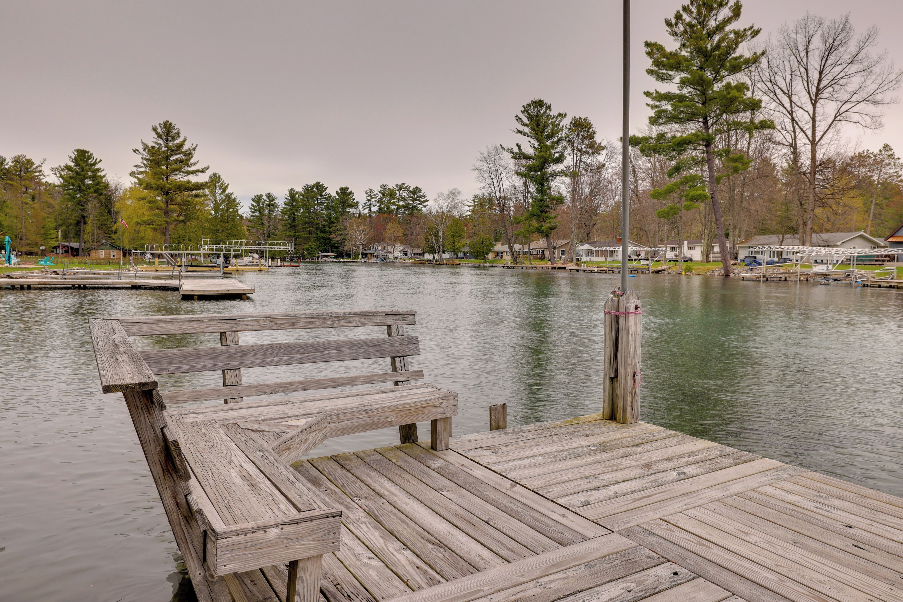 A wooden dock extending into a calm lake with a bench, surrounded by trees and houses.