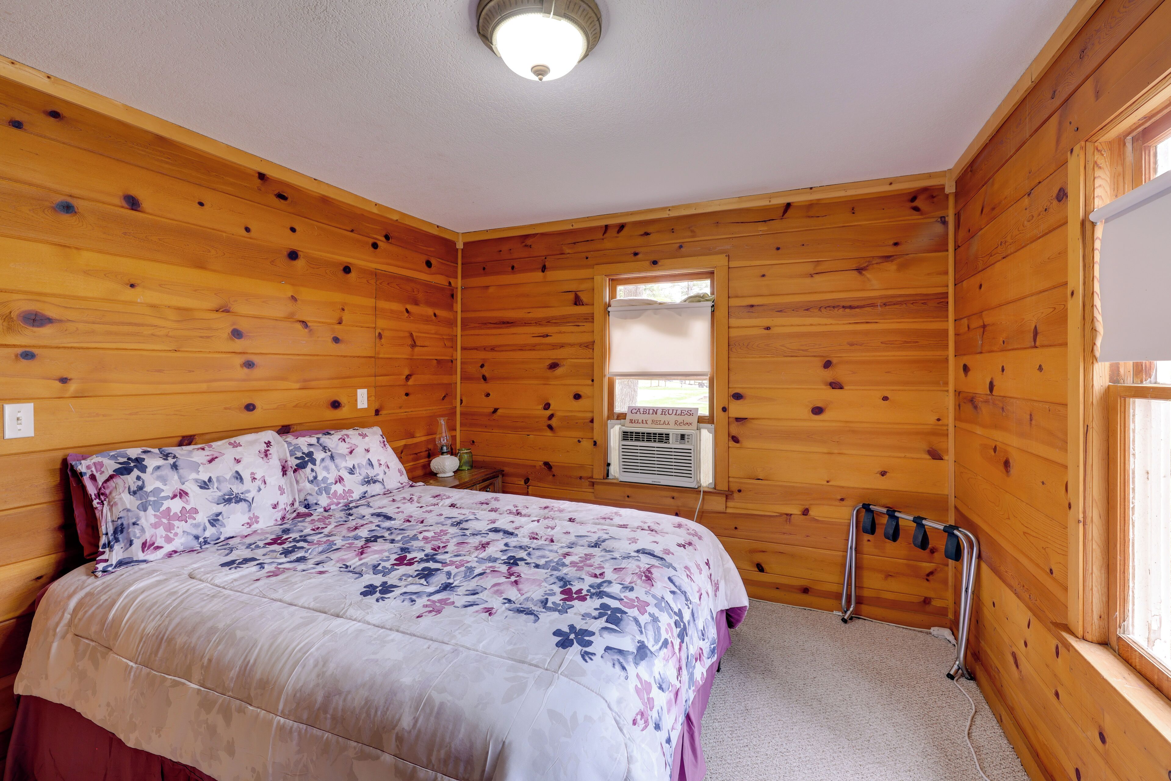 Ein Zimmer einer Holzhütte mit einem Bett, einem Fenster und einem Thermostat.