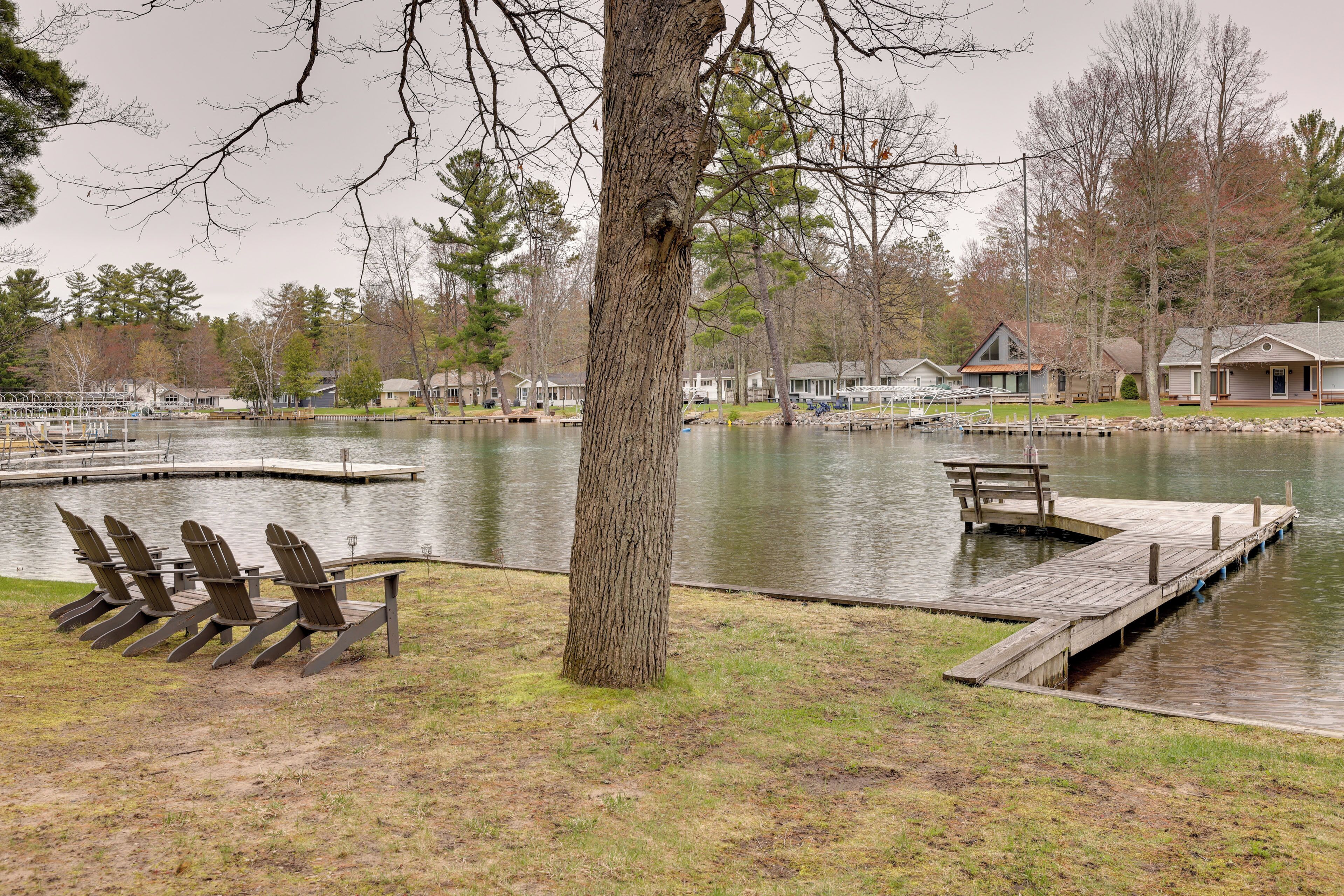 A lakeside view with docked boats, a row of chairs, and a large tree.