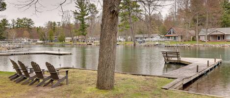 A lakeside view with docked boats, a row of chairs, and a large tree.