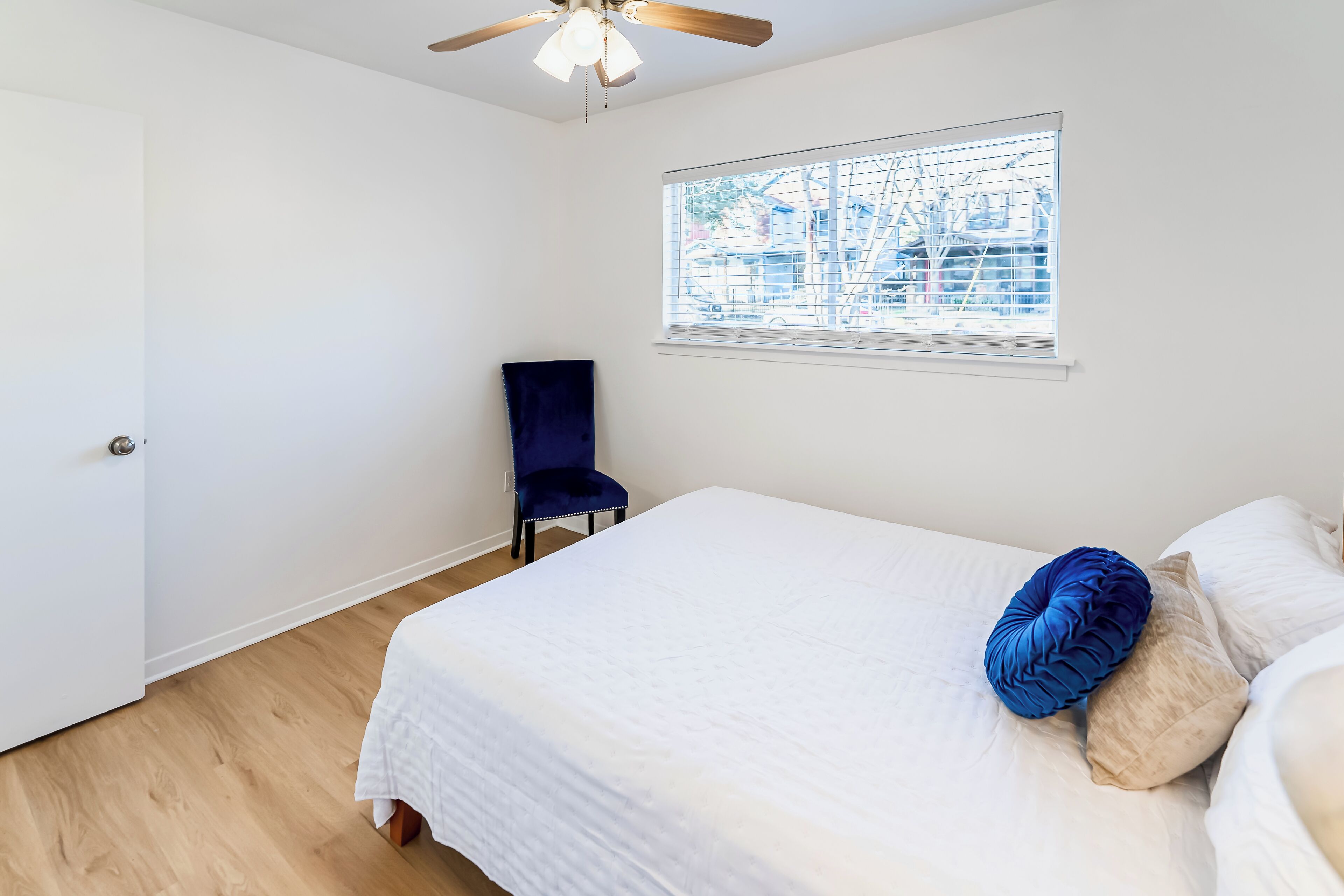 Un dormitorio con cama, una silla, una ventana con persianas y un ventilador de techo.