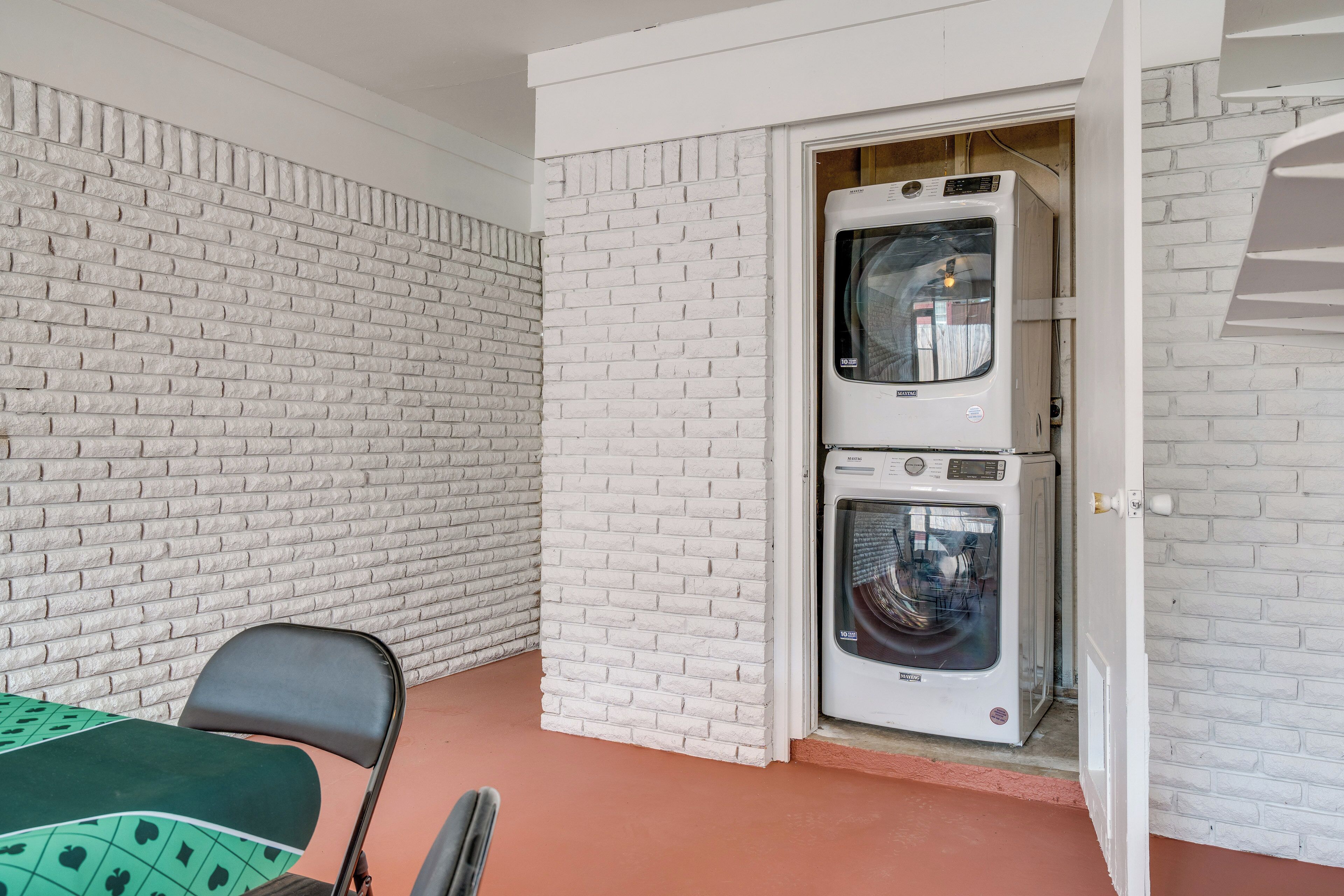 A laundry room with a white brick wall, a washing machine, and a folding table with chairs.