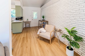 Une cuisine moderne équipée d’un four à micro-ondes, d’une petite table et d’une chaise. On y trouve un mur en briques blanches et une plante en pot.