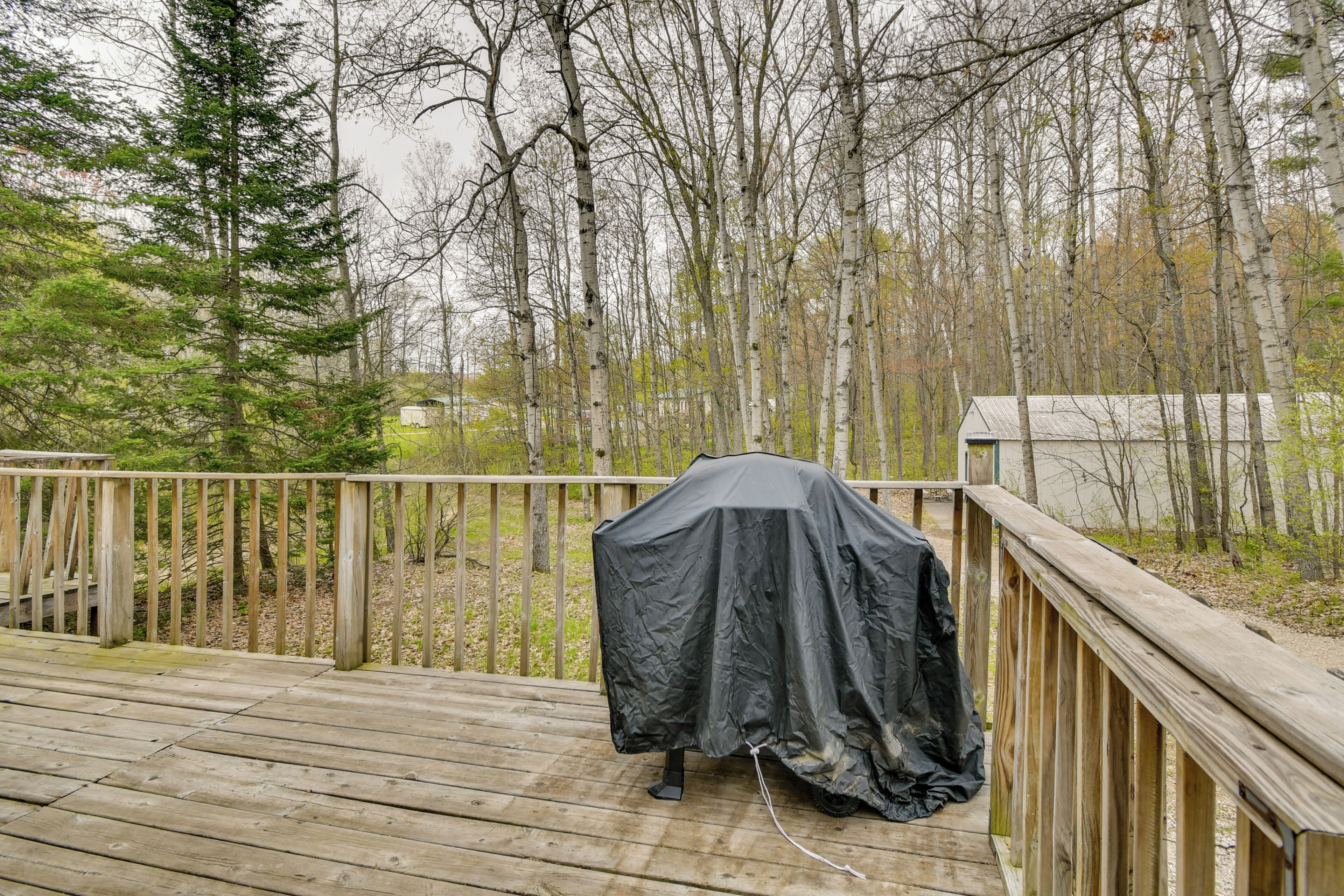 A wooden deck with a covered grill, surrounded by trees and a wooden fence.