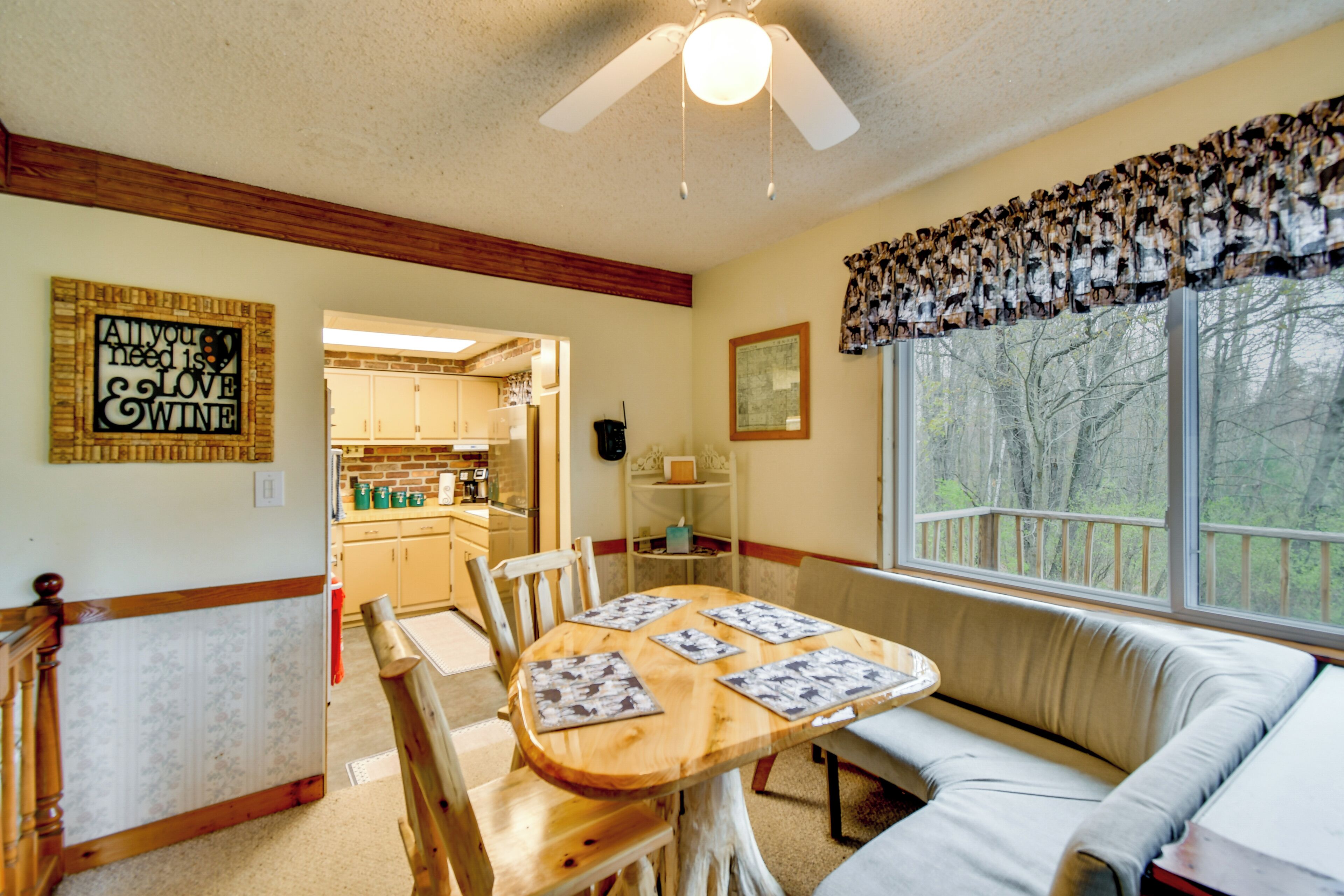 A dining area with a wooden table, chairs, a bench, and a window with a view of trees.