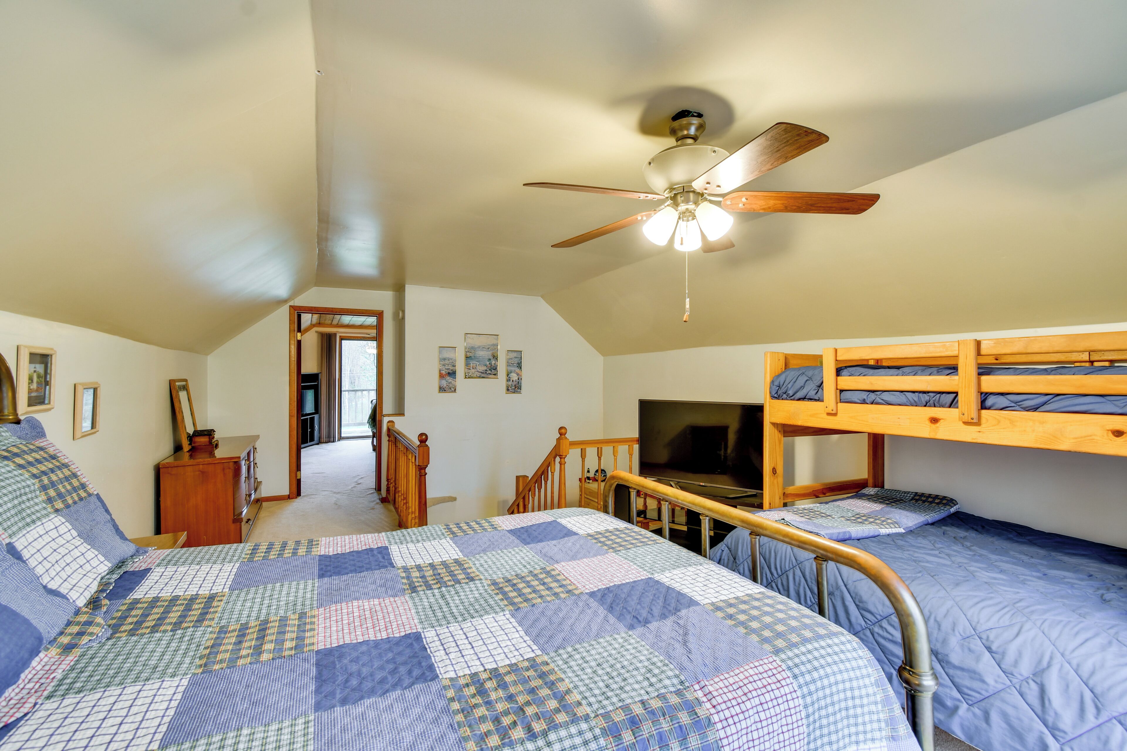 A bedroom with a bunk bed, a desk, a chair, a television, and a ceiling fan.