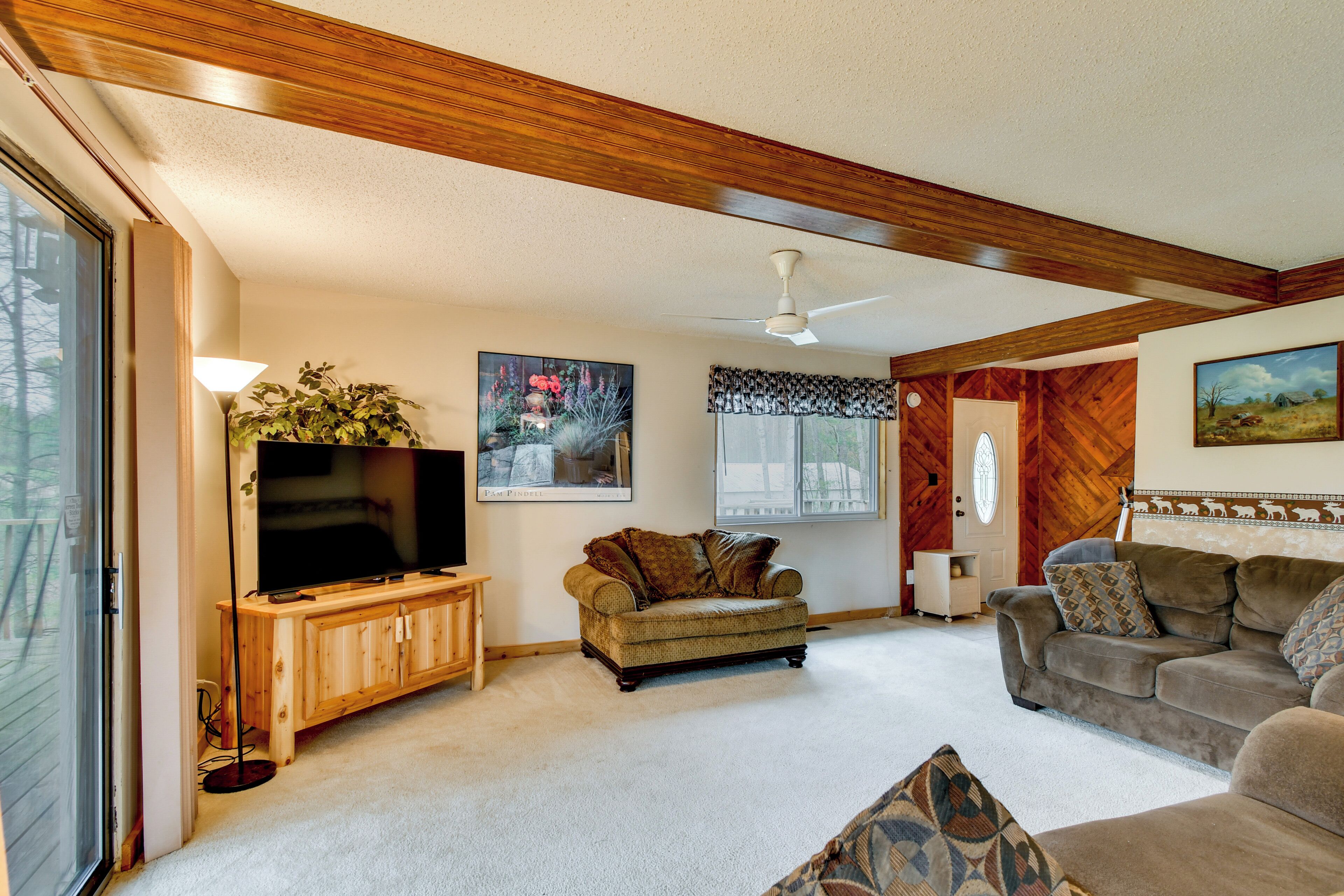 A living room with a television, wooden furniture, a ceiling fan, and a large window.