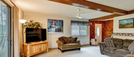 A living room with a television, wooden furniture, a ceiling fan, and a large window.
