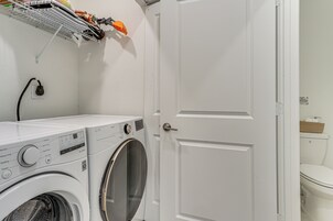 Un área de lavandería con lavadora y secadora, una puerta blanca y un estante con productos de limpieza.
