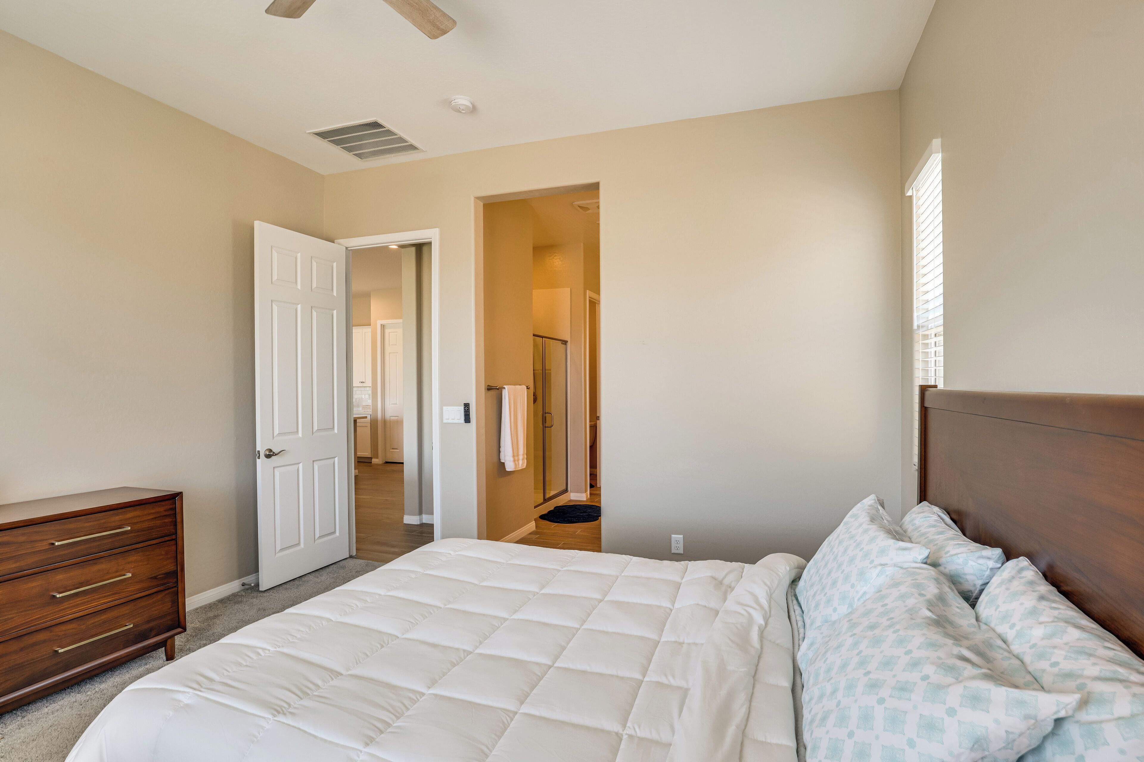 A bedroom with a bed, a dresser, a door leading to another room, and a window.