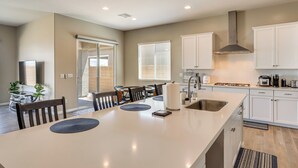 Une cuisine moderne avec des meubles blancs, un grand îlot central et un coin repas comprenant des chaises et une table.
