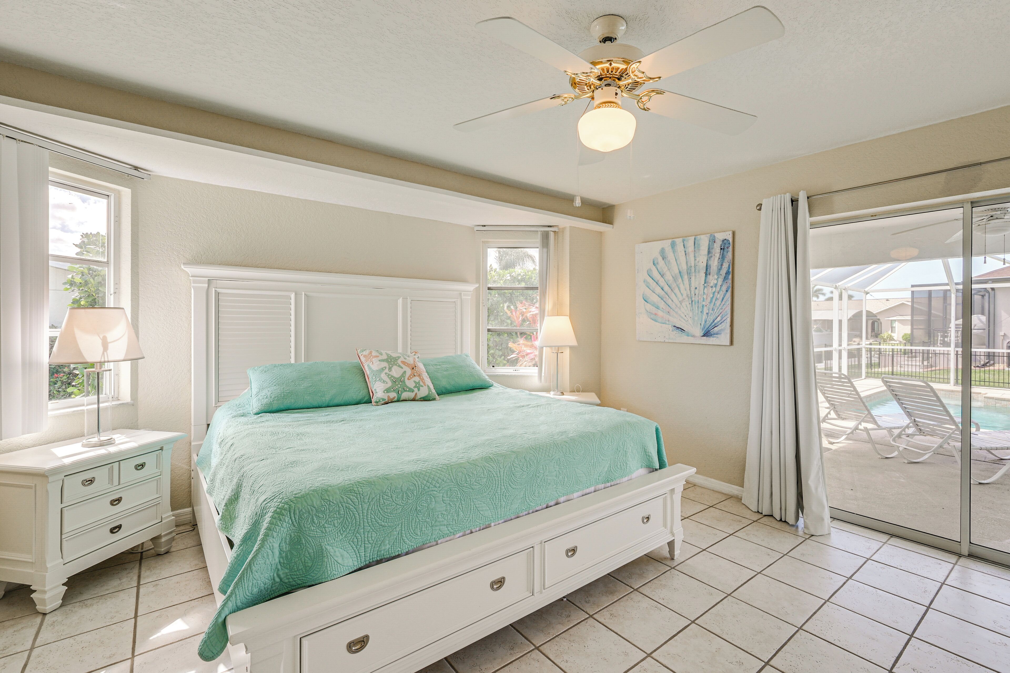 Ein Schlafzimmer mit Bett, Nachttischen, Deckenventilator und Blick auf einen Pool durch eine Glasschiebetür.