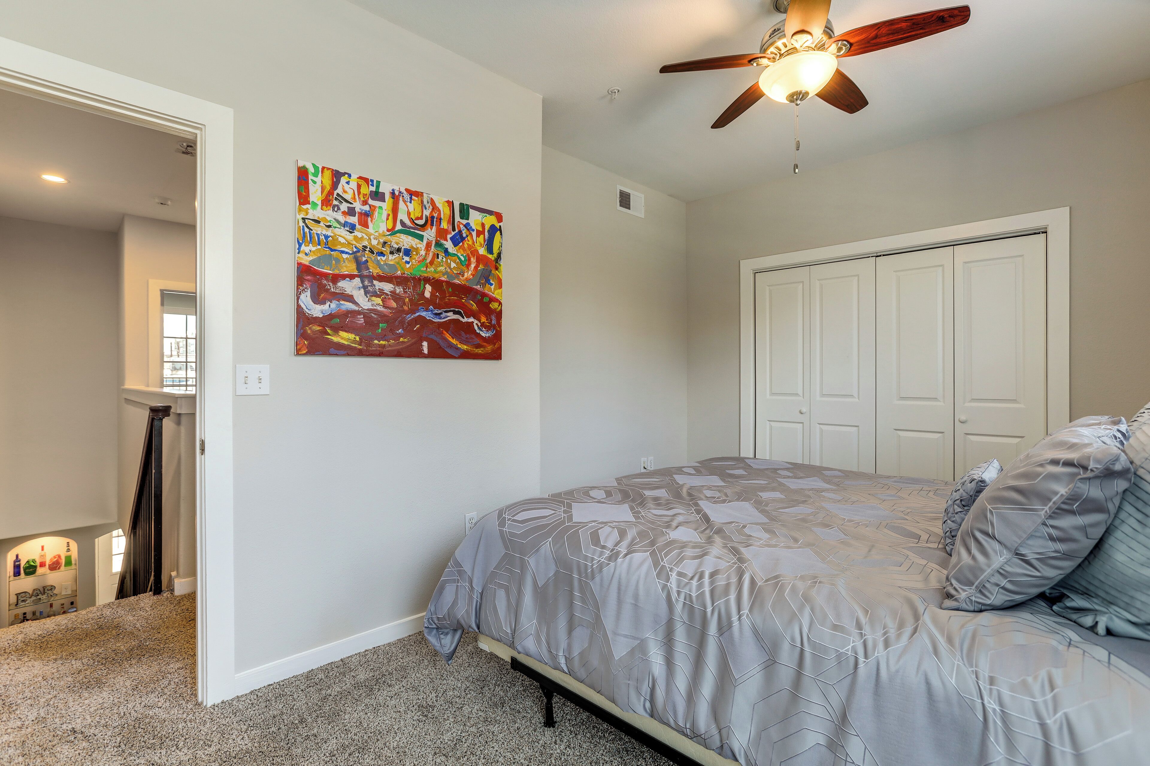 A bedroom with a bed, a ceiling fan, a door, and a painting on the wall.