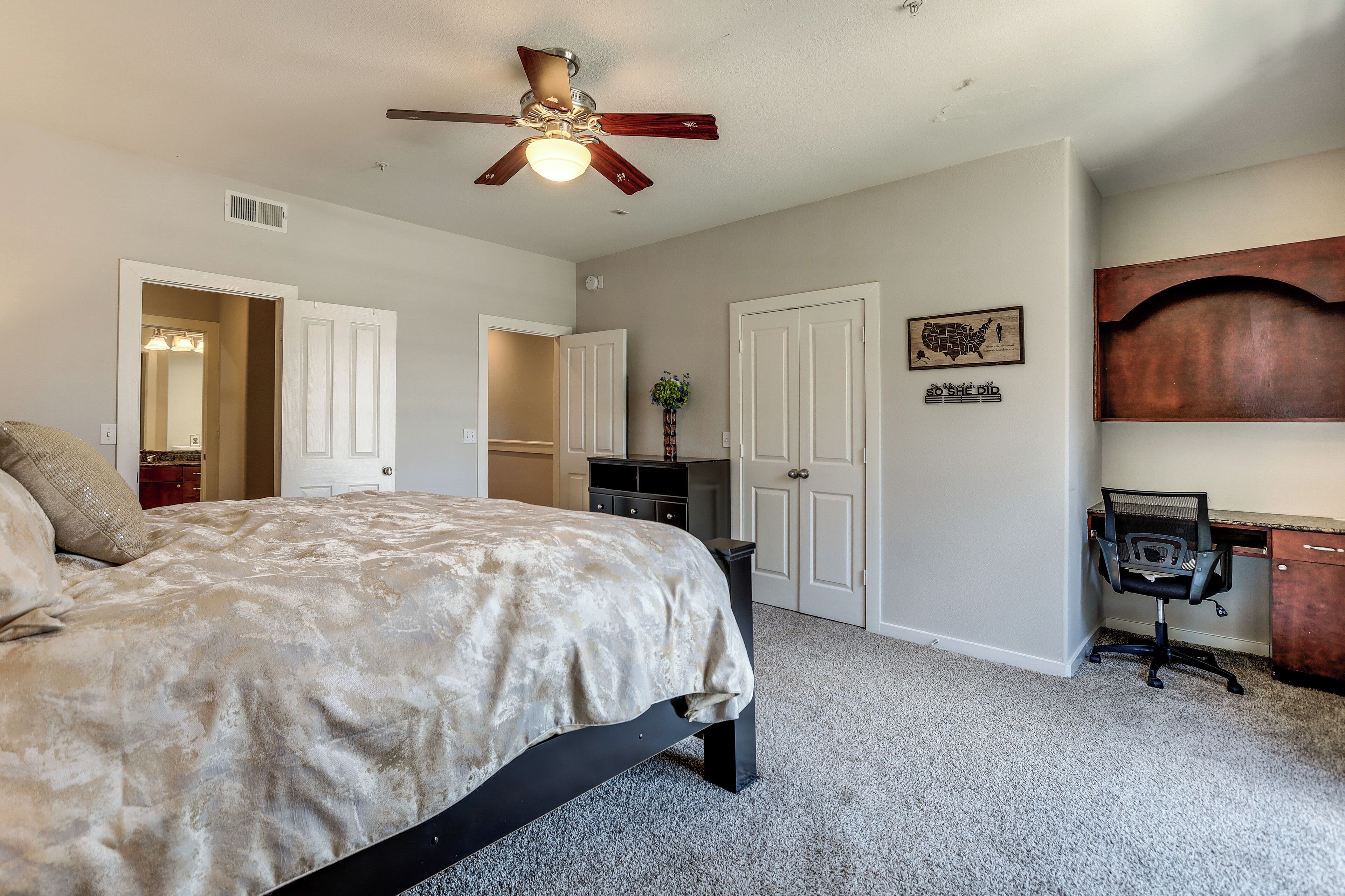 Une chambre à coucher comprenant un lit, un bureau, une chaise, un ventilateur de plafond et une porte.