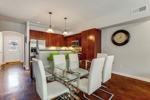 A modern kitchen with wooden cabinets, stainless steel appliances, and a dining area with glass tables and white chairs. - Walkable Eado Condo Near Dtwn: Modern + Chic! (Houston)