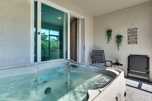 A hot tub with a clear view of the outdoors, a chair, a small table with a plant, and a wall-mounted sign. - Work & Play! Home w/ Modern Comfort in Estero (Estero)