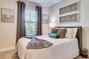 A bedroom with a bed, curtains, a window with blinds, a wall-mounted lamp, and two framed wall art pieces. - Work & Play! Home w/ Modern Comfort in Estero (Estero)