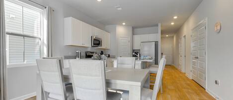 Una cocina moderna con armarios blancos, una mesa de comedor con sillas y suelo de madera.