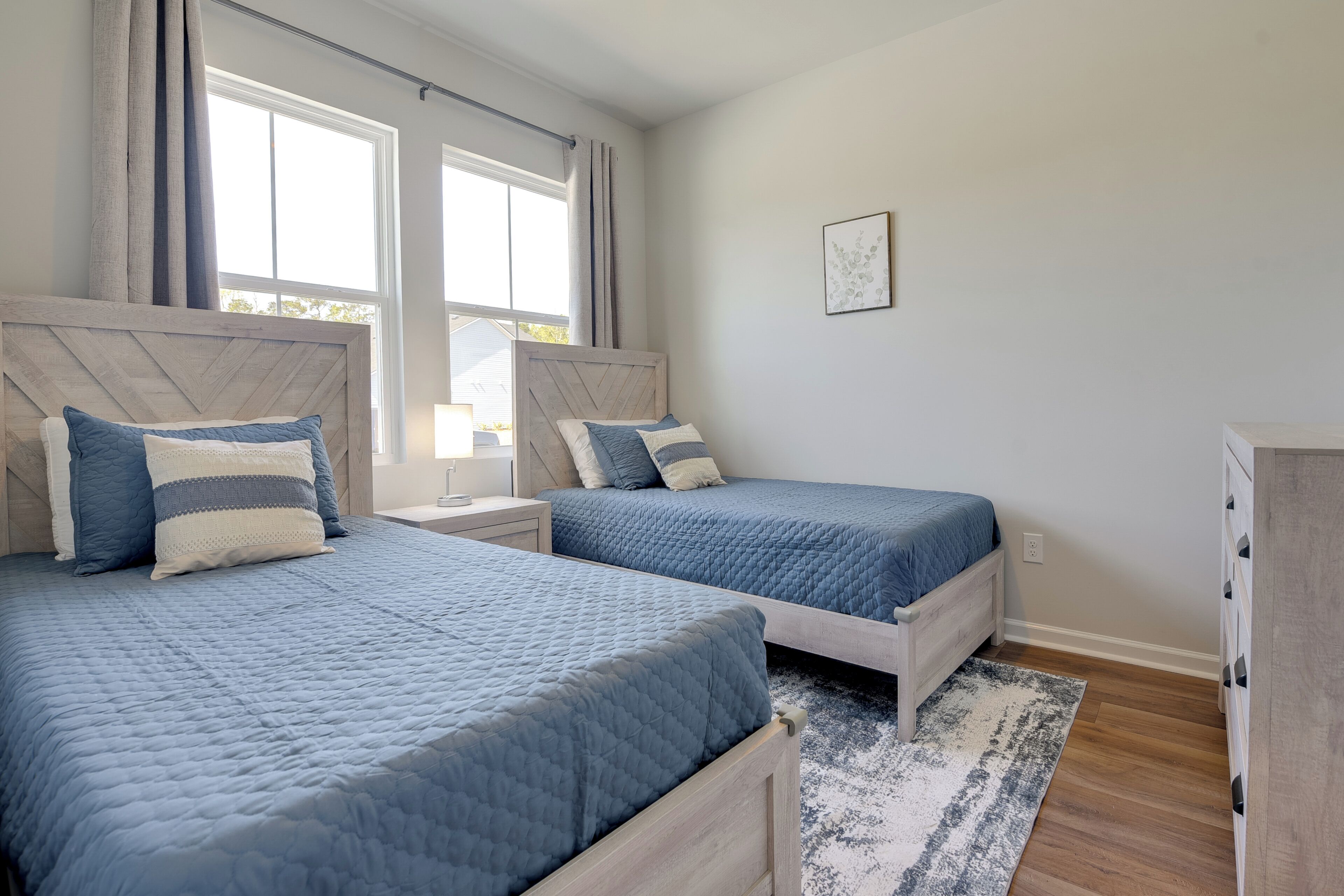 A bedroom with two beds, a nightstand, a dresser, and a window with curtains.