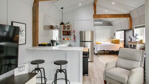 A modern kitchen with white cabinetry, a central island, and a dining area with a bar stool. - 6 Mi to Lake Pend Oreille! Cozy Cabins w/ Views (Athol)