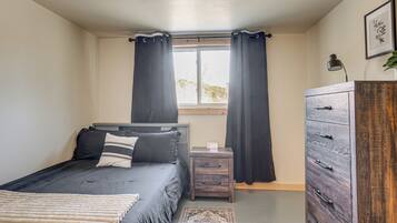 A bedroom with a bed, a nightstand, a dresser, a window with curtains, and a small rug.