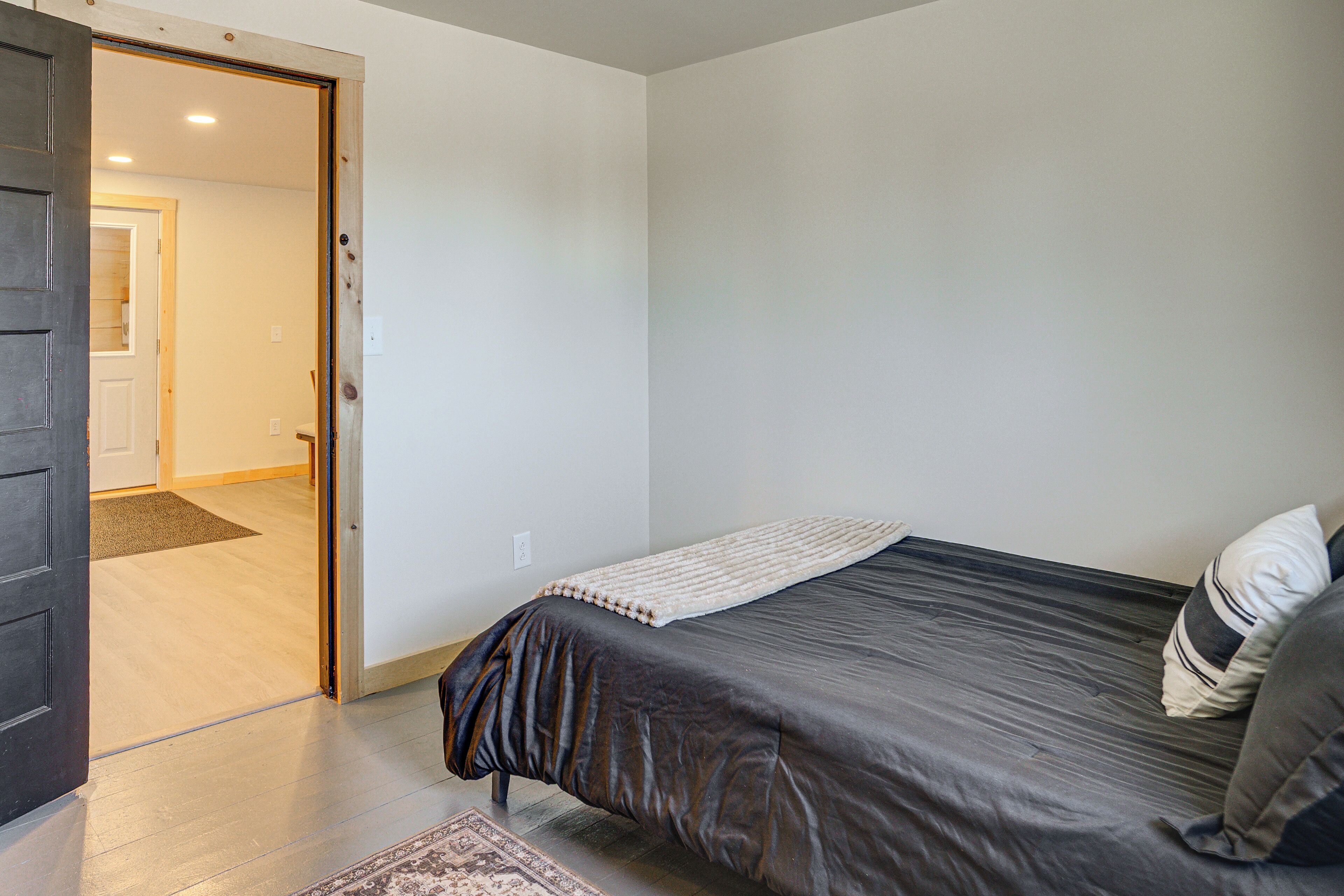 A bedroom with a bed, a door leading to another room, and a visible light switch on the wall.