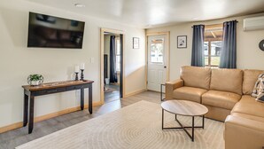 A living room with a sofa, a coffee table, a TV, a console table, and a door leading to another room.