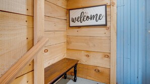 A wooden interior with a 'welcome' sign, a bench, and a blue door.