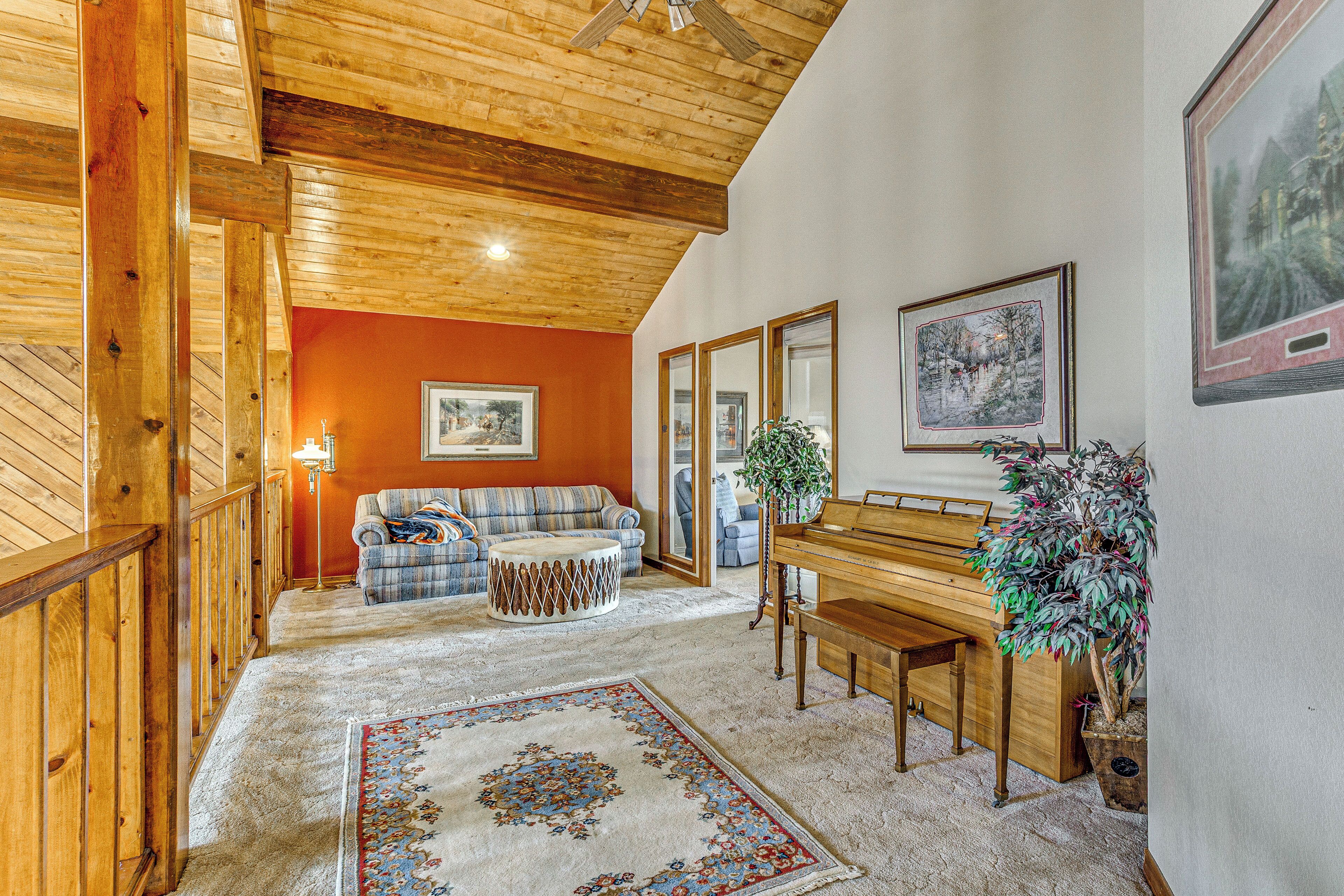 Una sala de estar con piso de madera, un sofá, un banco, un piano y una planta grande.