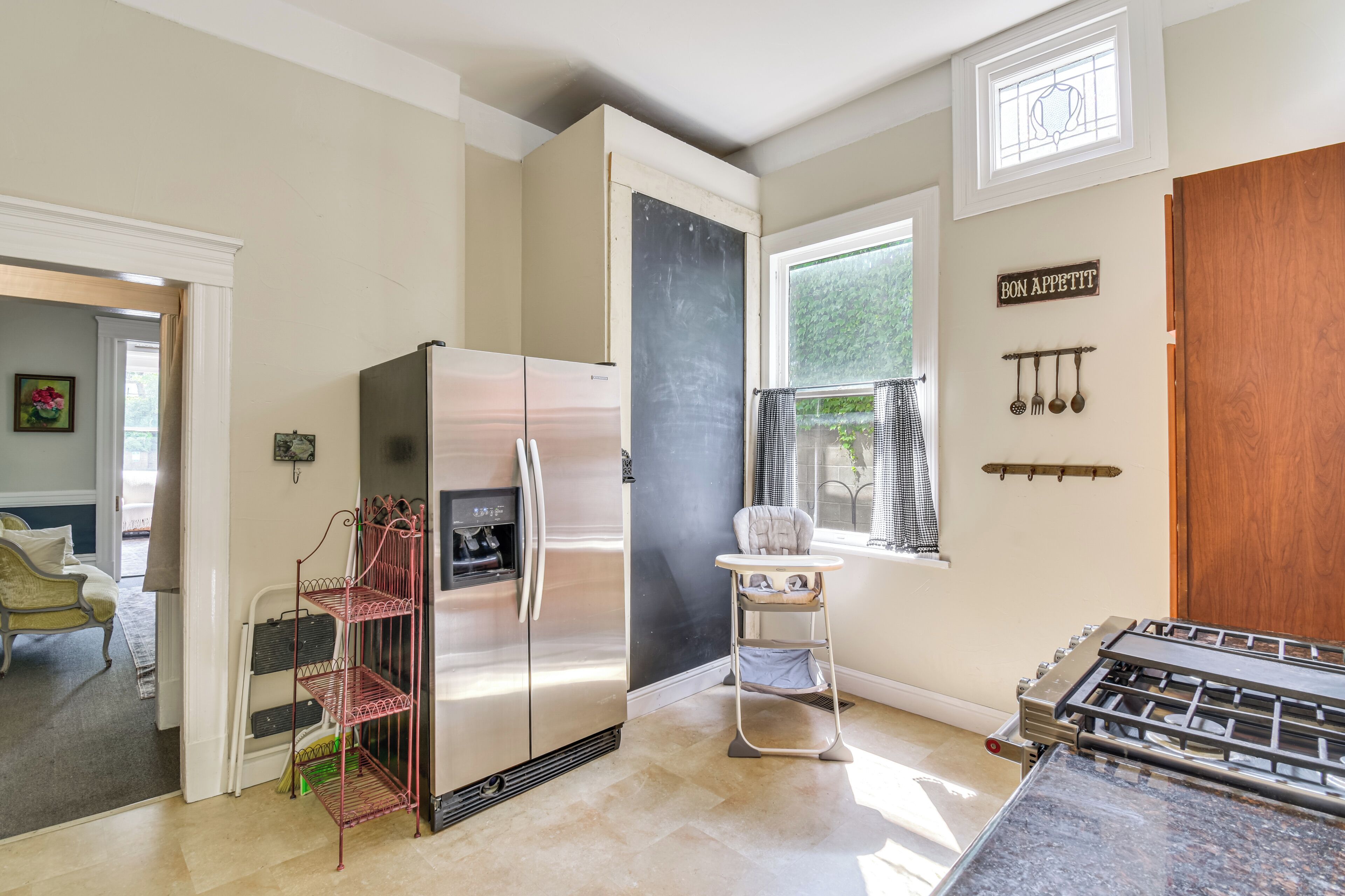 Una cocina con un refrigerador de acero inoxidable, una trona, una estufa a gas y una ventana con vistas a zonas verdes.