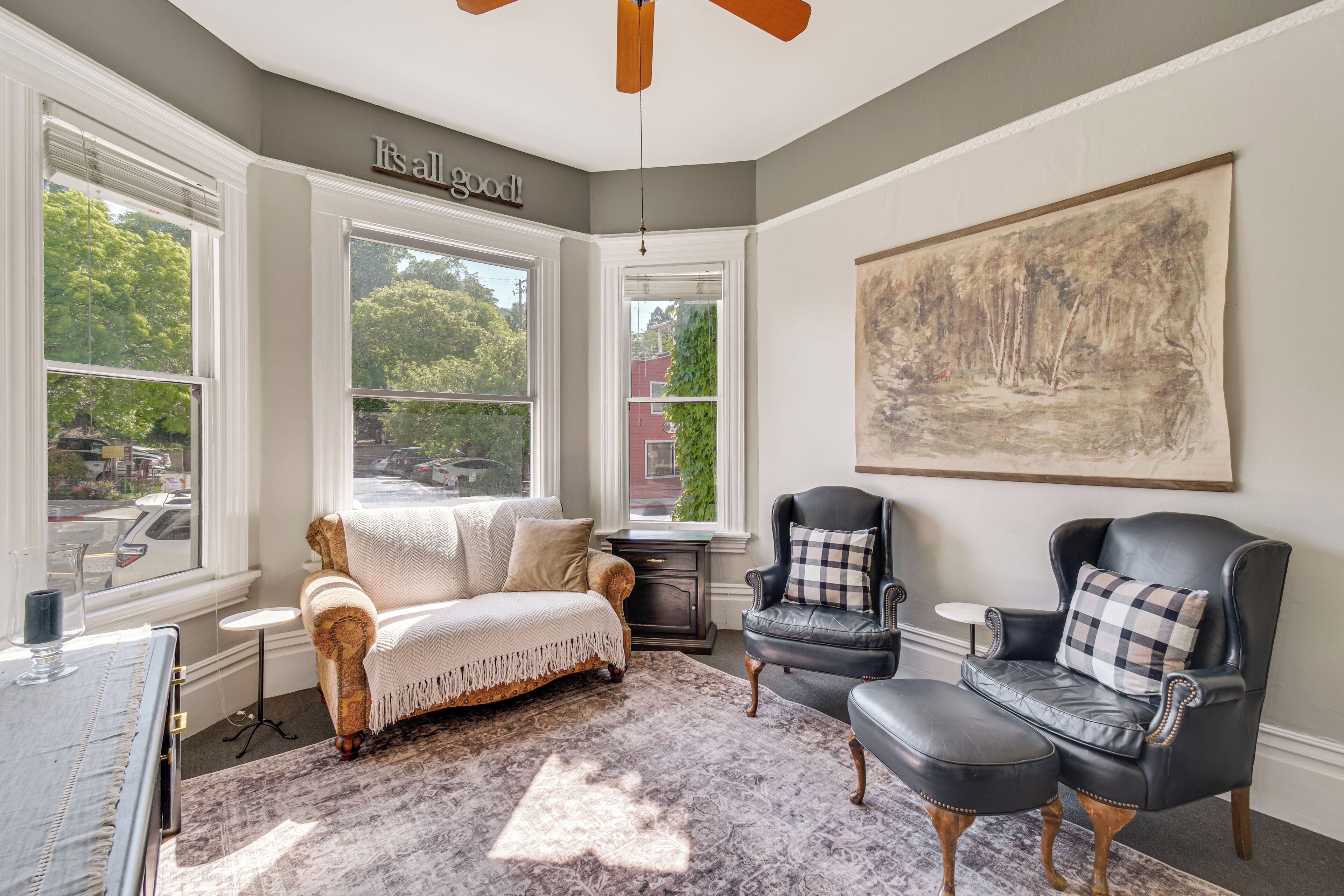A room with a sofa, a chair, a rug, and a painting on the wall.