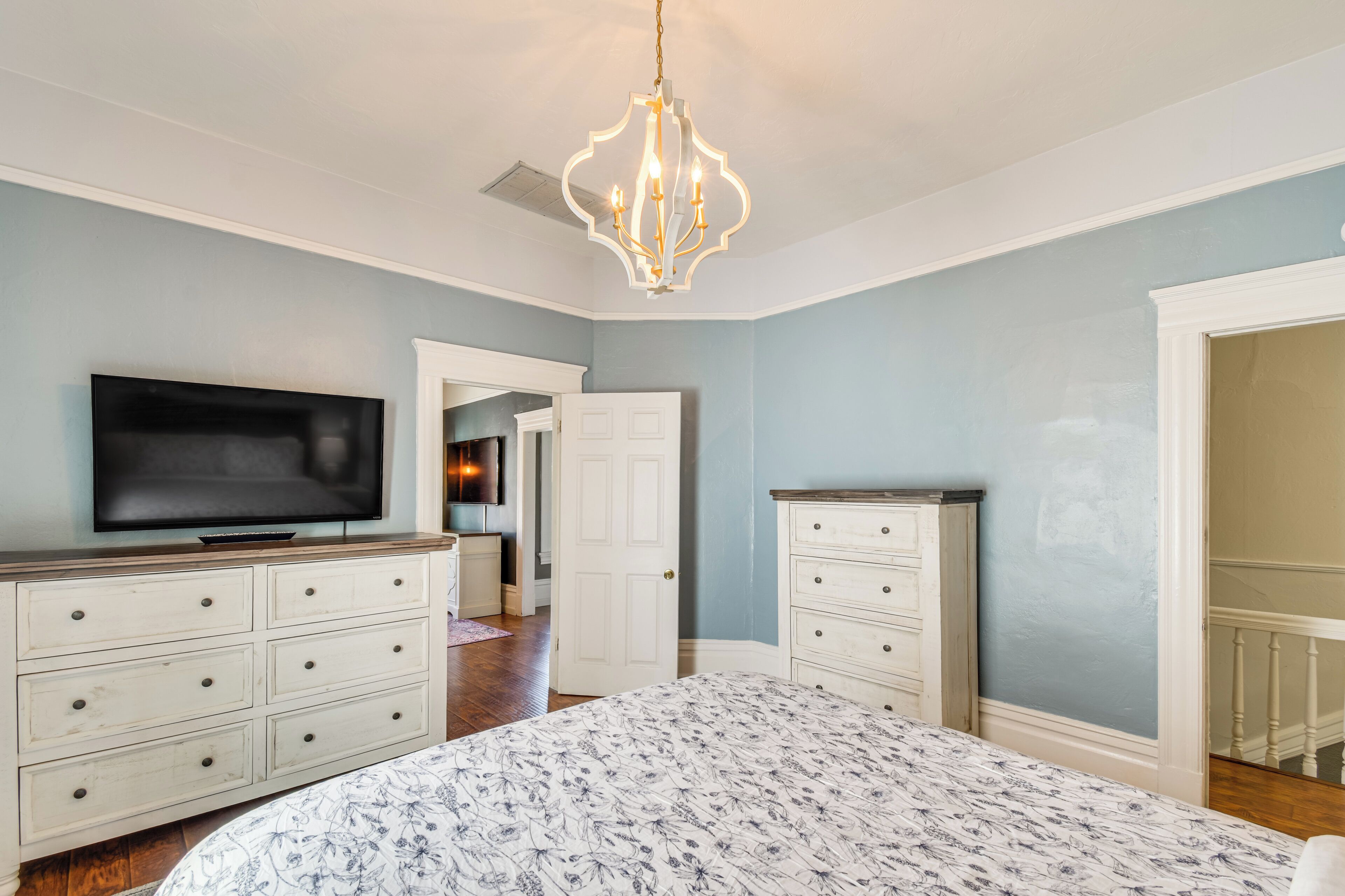 A bedroom with a bed, a television, a dresser, and a chandelier.