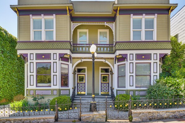 A two-story Victorian-style house with a front porch, a stone staircase, and a decorative fence.