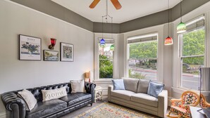 A living room with a black leather sofa, a beige sofa, a patterned rug, and a rocking chair. - Historic Home in Downtown Sonora! (Sonora)